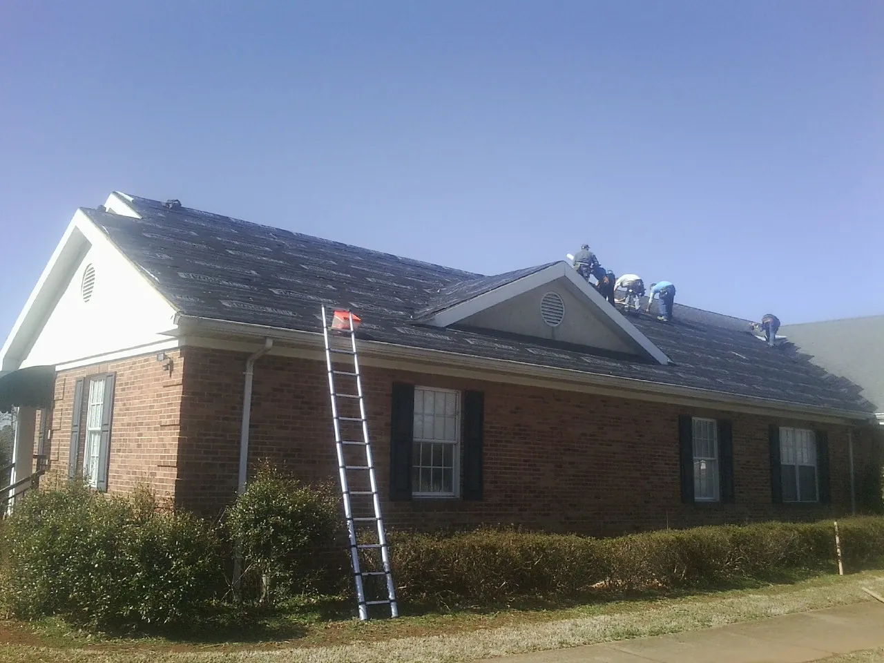 Crew tearing shingles off a brick ranch roof with a ladder set — Metal Roof Repair work by our crew in White Post