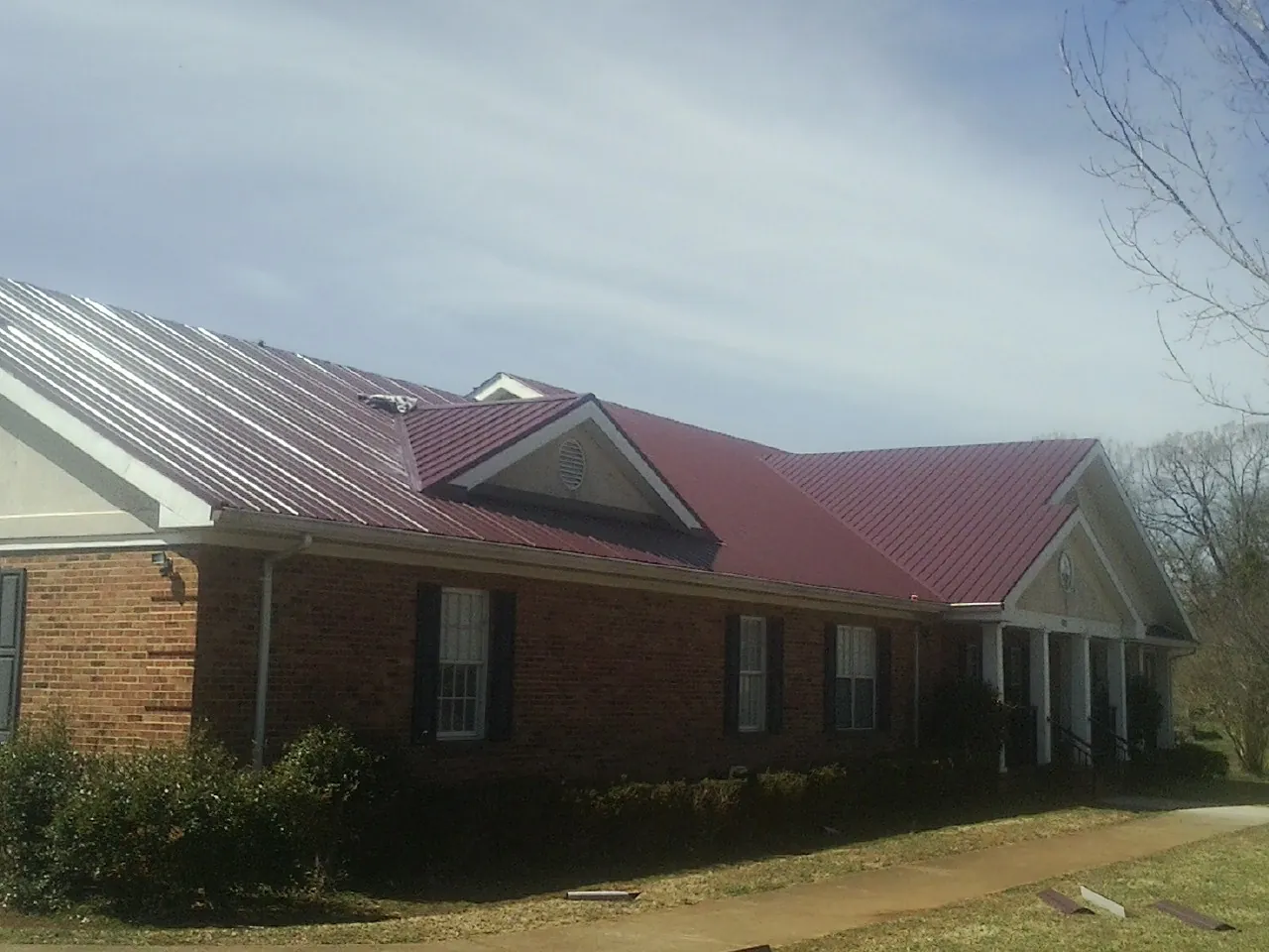 Red metal roof with gabled entries on a long brick building, from a Hail Damage Roof Repair job in White Post