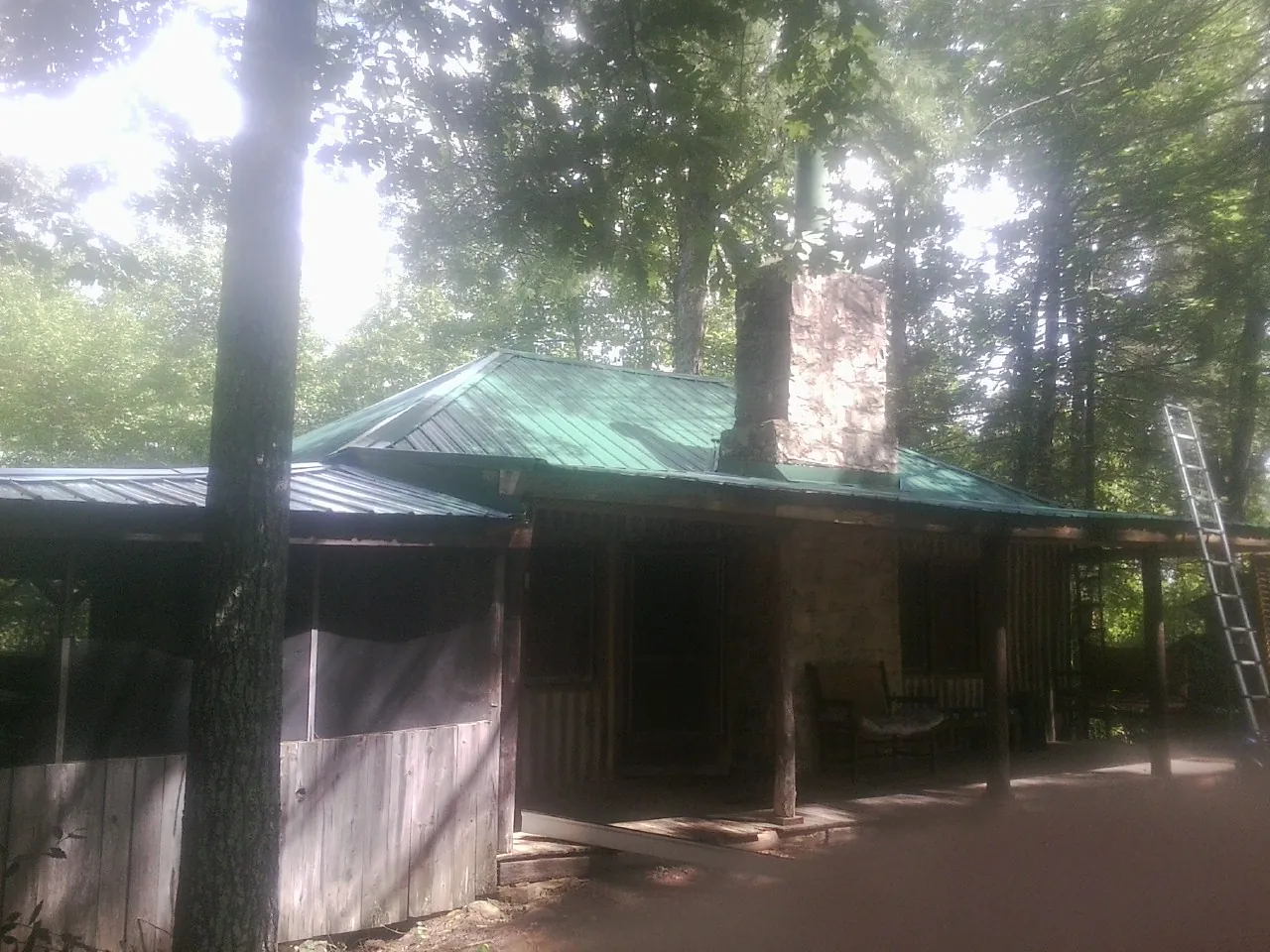 Green metal roof and stone chimney above a log cabin porch in White Post