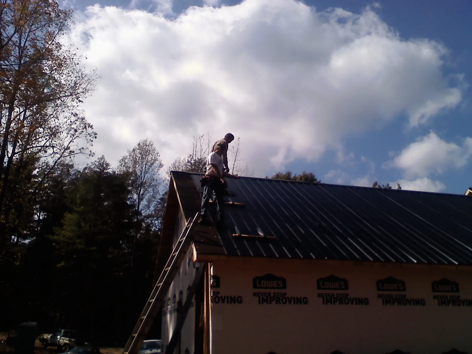 Roofer fastening dark metal panels high against a cloudy sky, from a Roof Inspection job in White Post